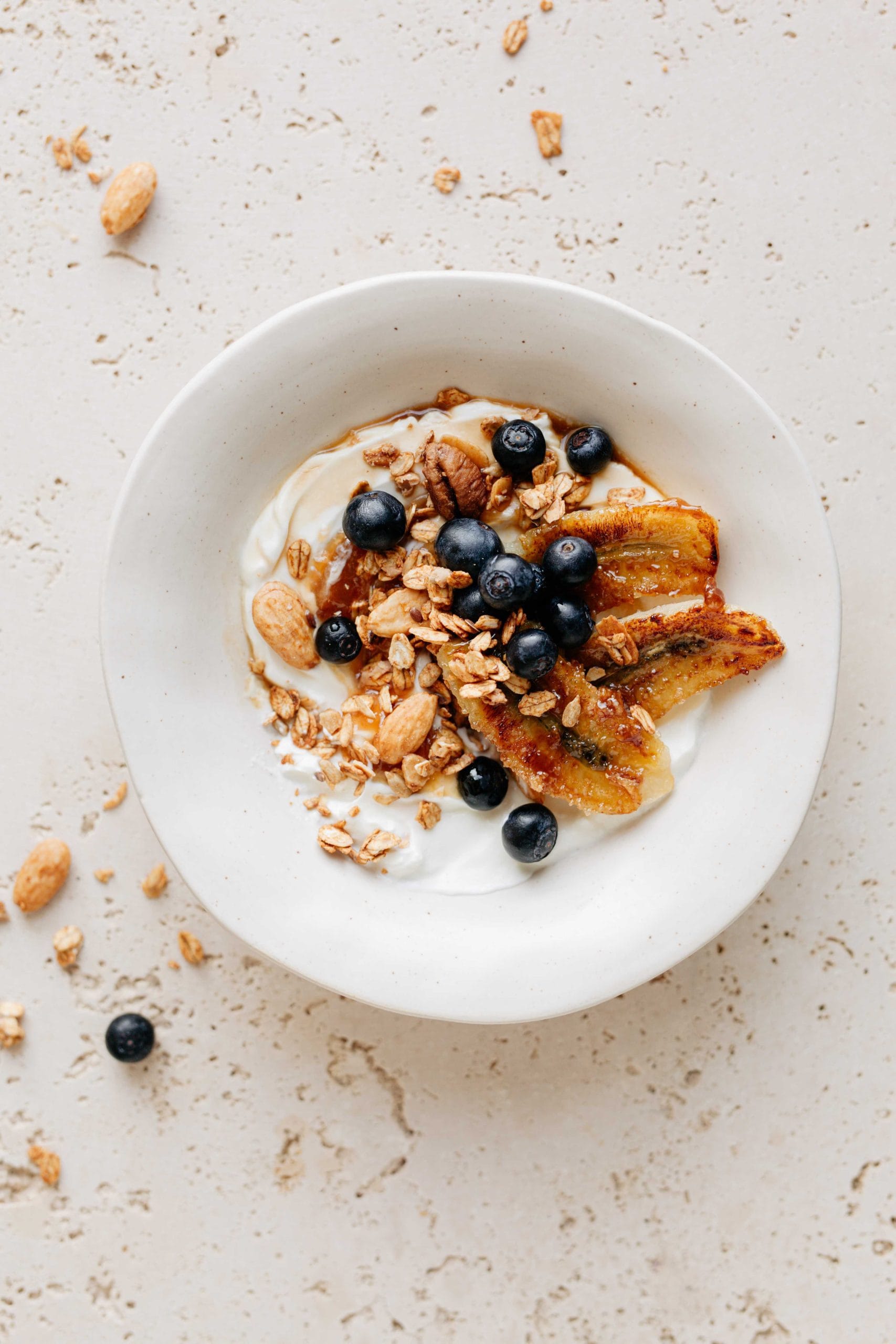 miseczka z migdałami, orzechami pekan podana z jogurtem, pieczonymi bananami i borówkami.