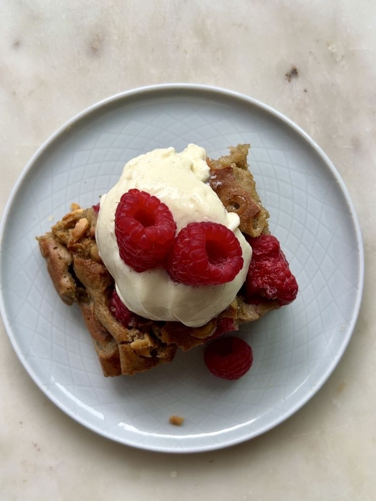 Jasny talerzyk na blacie, na talerzyku kawałek ciasta – pieczona owsianka z malinami i białą czekoladą