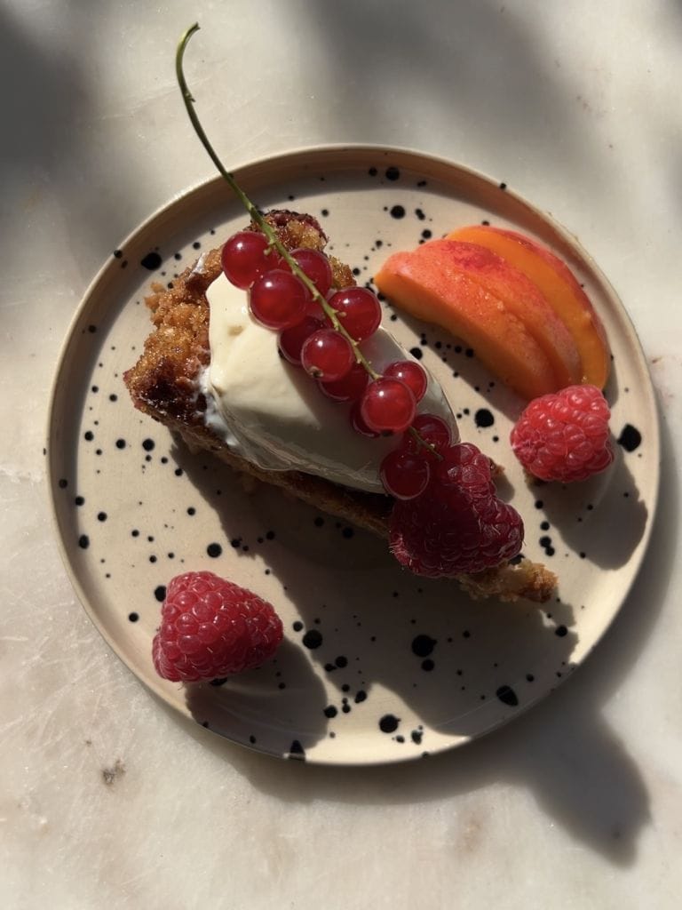 Talerzyk na blacie, a na talerzu świeże owoce oraz kawałek ciasta orzechowego – jedna z propozycji na hasło śniadanie na upały